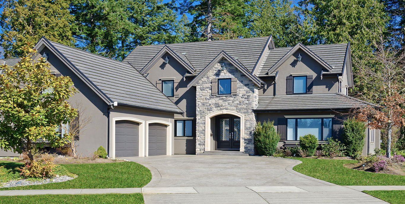 Elegant home exterior with gray painted walls, gray garage doors, stone decor for the front door, and a big alley in front of the house.
