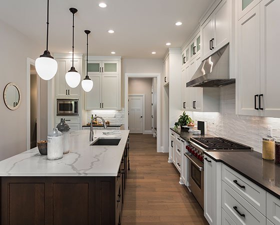 Modern, elegant kitchen with white cabinets, silver finish appliances, dark wooden island, and beige quartz countertop.