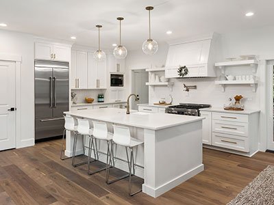 Large kitchen with white painted cabinets, large island with wood and quartz countertop, dark brown flooring, and silver finish appliances.