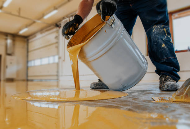 Worker applying a yellow epoxy resin bucket on floor.