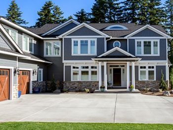 House exterior with navy blue siding, stone decor for the base, wooden garage doors, and white windows.