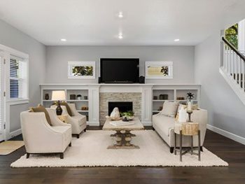 Small living room with light gray painted walls, light beige couch and carpet, stone chimney, flat screen TV, and stairs on the right side.