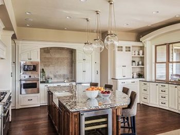 Luxury kitchen with large, brown island, quartz countertop, silver finish appliances, and white painted cabinets.